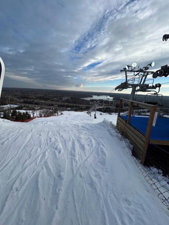 The view from the top of Buck Hill on a bright day, the chairlift on the right and the Twin Cities plain, a lake and a highway spread out below.