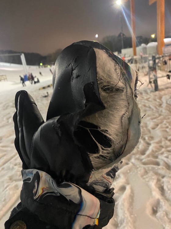 A leather mitten worn through at the palm with the lining pulled out, held up at night with the lit hill behind.