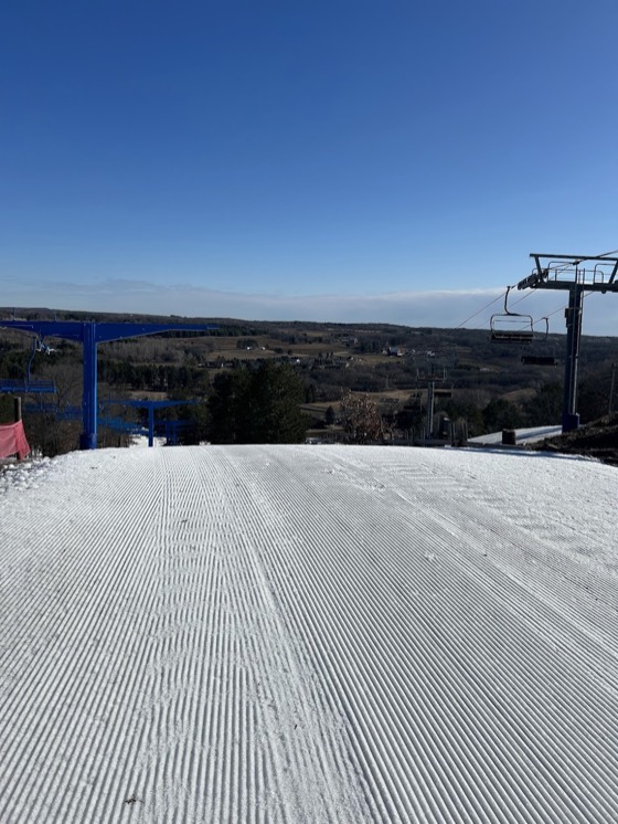Fresh corduroy at the top of a run at Trollhaugen, blue lift towers either side and Wisconsin farmland in the valley below.