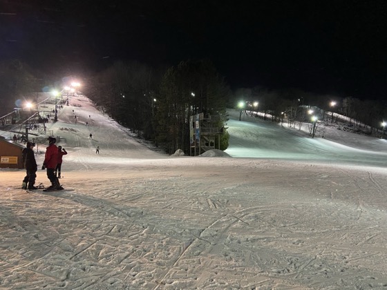 Wild Mountain under the lights at night, the chairlift running and tracked-out snow across the base area.