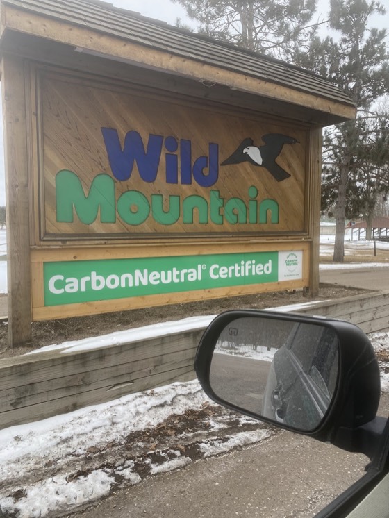 The wooden entrance sign at Wild Mountain, the name in blue and green with an eagle, and a CarbonNeutral Certified banner beneath it.